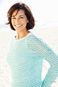 Brunette woman wearing white top and loosely knitted mint sweater on beach