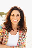 A brunette woman on a beach wearing a white top and colourful cardigan