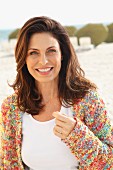 A brunette woman on a beach wearing a white top and colourful cardigan