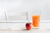 A glass of fruit juice and an apple on a white wooden table with a chair