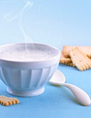 A bowl of hot milk with a bowl and biscuits next to it
