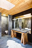 Designer bathroom with washstand on rustic wooden trestles, grey tiles and skylight shaft in wooden ceiling