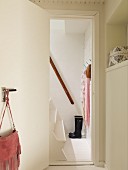 Blick durch geöffnete Tür auf weiß lackierte Holzstiege mit Handlauf, schwarze Gummistiefel und Tücher an Wandhaken