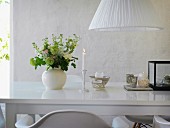 Romantic arrangement of lit candle and vase of flowers on glossy white table