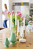 weiße Kerzen mit Messing und Keramik Kerzenhalter vor Frühlingssträussen, im Vordergrund Salzstreuer in Grün auf Holztisch
