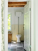 Blick durch offene Tür auf Toilette auf grauem Fliesenboden, in ländlichem Bad
