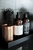 Copper-coloured metal beaker and soap dispenser on black shelf