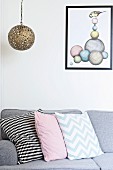 Patterned scatter cushions arranged on grey sofa below pendant lamp with spherical metal lampshade