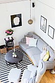 View down onto grey sofa set, round coffee table and black and white striped rug in corner of living room