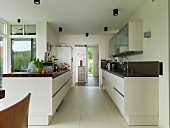 Gegenüberliegende Küchenzeilen in offener Küche mit grossformatigem Fliesenboden, im Hintergrund Durchgang mit Blick in Eingangsbereich