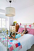 Children reading on pretty bed with patchwork cover in vintage-style girl's bedroom
