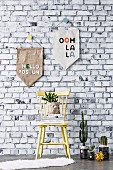 Homemade pennants in front of wallpaper with a brick wall motif, in front of a wooden chair and cacti