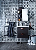 Towel rail and sink with black base unit below mirrored cabinet hung on wall with black and white tile-patterned wallpaper