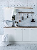 White base units, washing-up brushes hung from hooks and clothes airer suspended from ceiling in utility room with brick-patterned wallpaper