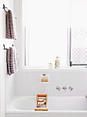 Bathtub with toiletries in wooden bath caddy below brown and white stripes towels on towel rails