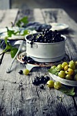 Blackcurrants and gooseberries in bowls on a wooden surface