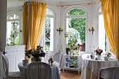 Set bistro tables in front of arched windows with yellow curtains in grand window bay