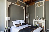 Double bed in bedroom with Baroque elements: stucco elements, some gilded, on grey-painted walls