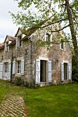 Rustic stone country house with white shutters and window in summer garden