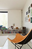 Butterfly chair with pale brown leather cover in front of half-height fitted bookshelves