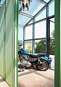 Blaues Motorrad im Glashaus mit grünem Raumteiler