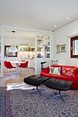 Glass sliding doors between dining area and living area; red designer couch and black leather footstools