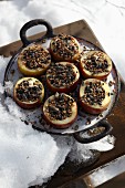 Halved apples filled with bird food in pan in snow