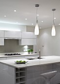 Bottle-shaped pendant lamps above sink unit with breakfast bar in designer kitchen