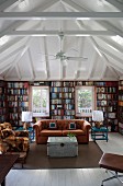 U-shaped bookcase in square room with pavilion roof structure; retro seating in natural shades in centre