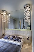 Französisches Bett mit gepolstertem Kopfteil und Fotokissen, darüber mondäne Bubble-Leuchten und Spiegelfront