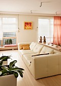 Cream leather sofa and potted orchids without flower spikes; windows with Roman blinds in background