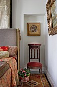 Ikonenbild und antiker Stuhl in Wandnische neben einem Bett mit Kopfpolster und traditionell gemusterten Stoffen