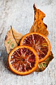 Two slices of caramelised blood-orange slices and dried leaved on wooden surface