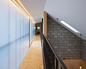 Narrow gallery with metal balustrade and frosted glass wall; open-plan, double-height interior with sloping ceiling to one side