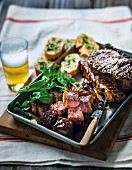 Grilled marinated beef steaks with garlic bread, salad and beer