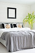 Pale grey blanket and scatter cushions with gold CND symbols on double bed; potted plant against white wood-clad wall to one side