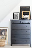 Picture and picture frame on top of black-painted chest of drawers under sloping ceiling