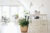 White counter and stools next to plant in wicker planter on pale floor and lounge area in background in converted attic