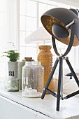 Table lamp with black and gilt lampshade next to vintage glass and ceramic vessels