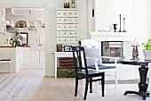 Round black table and chairs in front of fireplace next to wide, open doorway with view into kitchen