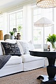 Black round table and white sofa with scatter cushions in front of standard lamp with white fabric lampshade