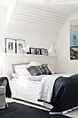 Double bed with black and white bedspread in attic room with wood-clad sloping ceiling