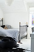 Vintage metal bed with grey bedspread in attic room with white, wood-clad sloping ceiling