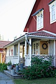 Veranda mit weißem Holzgeländer vor rotbraun gestrichenem Holzhaus