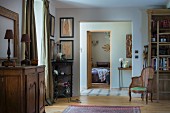 Table lamp on antique, rustic cabinet, antique cane armchair and doorway leading into bedroom