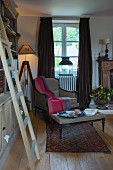 Living room with wooden ladder next to bookcase, standard lamp, armchair below window and floor-length curtains