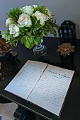 Aufgeschlagenes Tagebuch vor weißem Rosenstrauss in Glasvase
