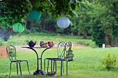 Curved metal table and chairs below lanterns hung in chestnut tree