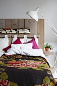White retro standard lamp next to bed with vintage-style bedspread and headboard made from reclaimed boards