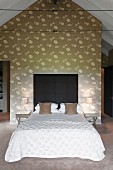 Double bed with dark headboard against wall with floral pattern